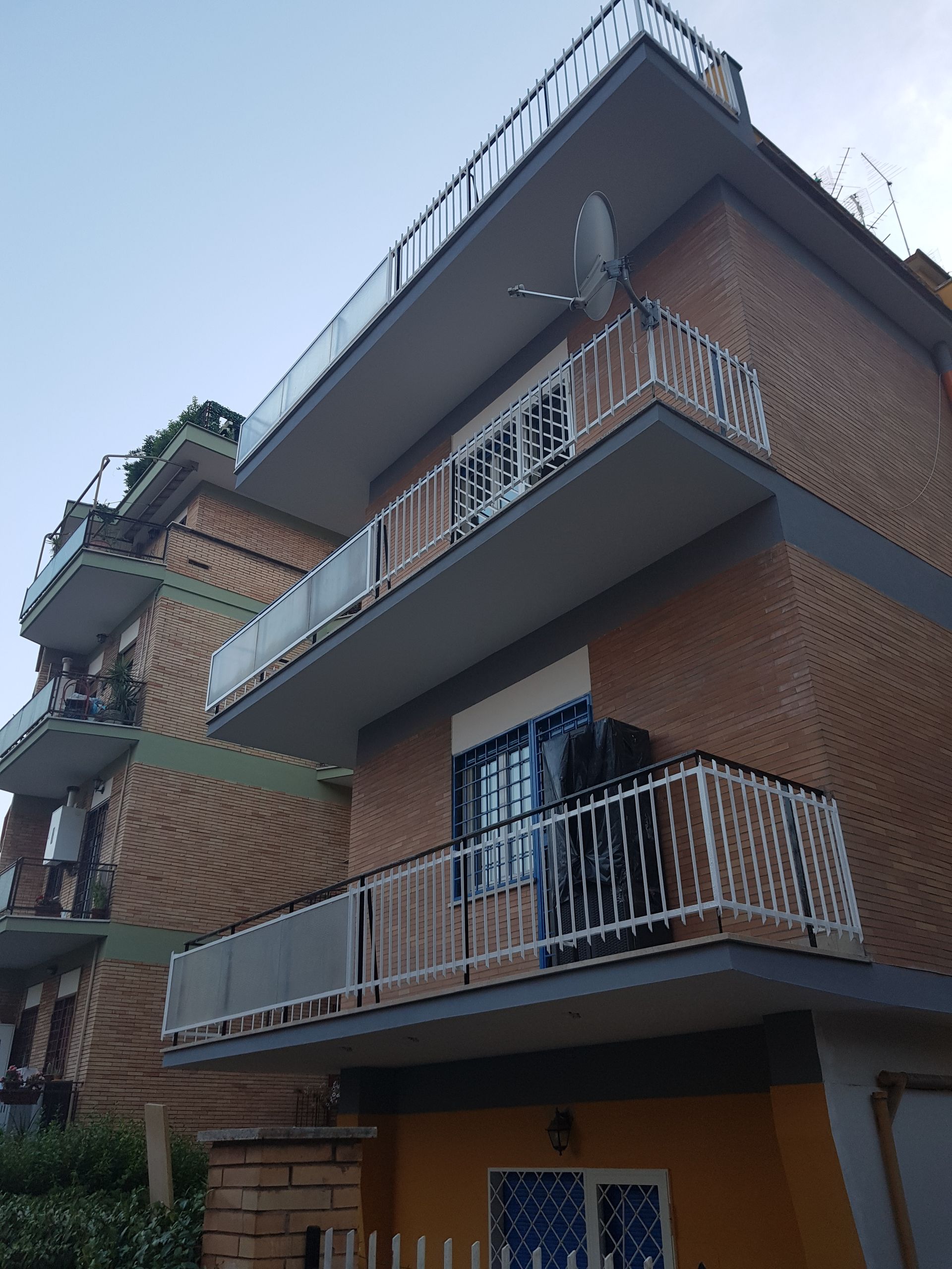 Balconi su un palazzo di mattoni a più piani con ringhiere in metallo e un cielo limpido sopra.