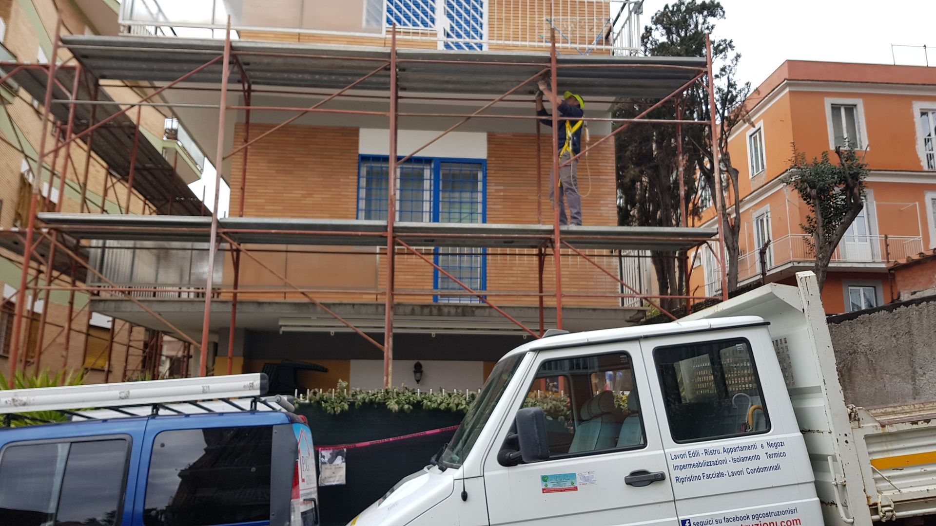 Edificio in mattoni con impalcature, in fase di ristrutturazione, con un camion bianco parcheggiato davanti.