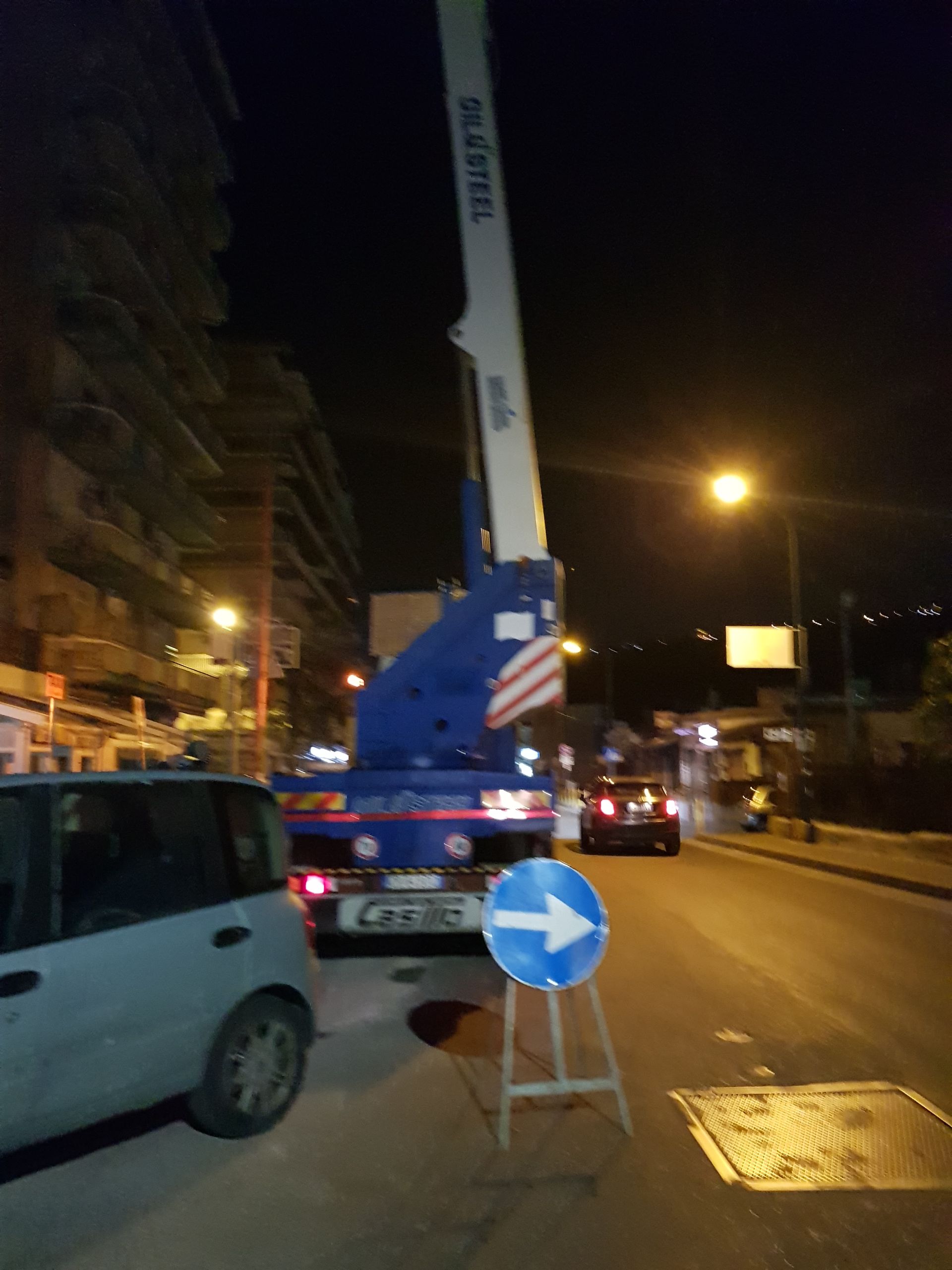 Strada notturna con un camion gru, coni stradali e un segnale blu di svolta a destra.