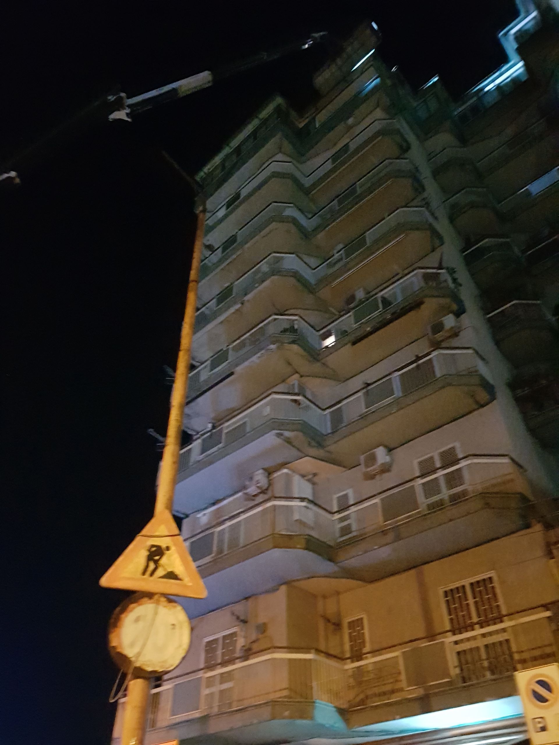 Veduta notturna di un alto condominio con balconi e un cartello stradale in primo piano.