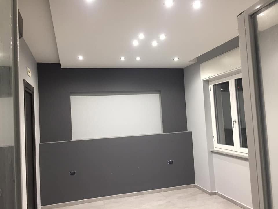 Stanza moderna e vuota con pareti grigie, faretti a incasso sul soffitto e un'ampia finestra.