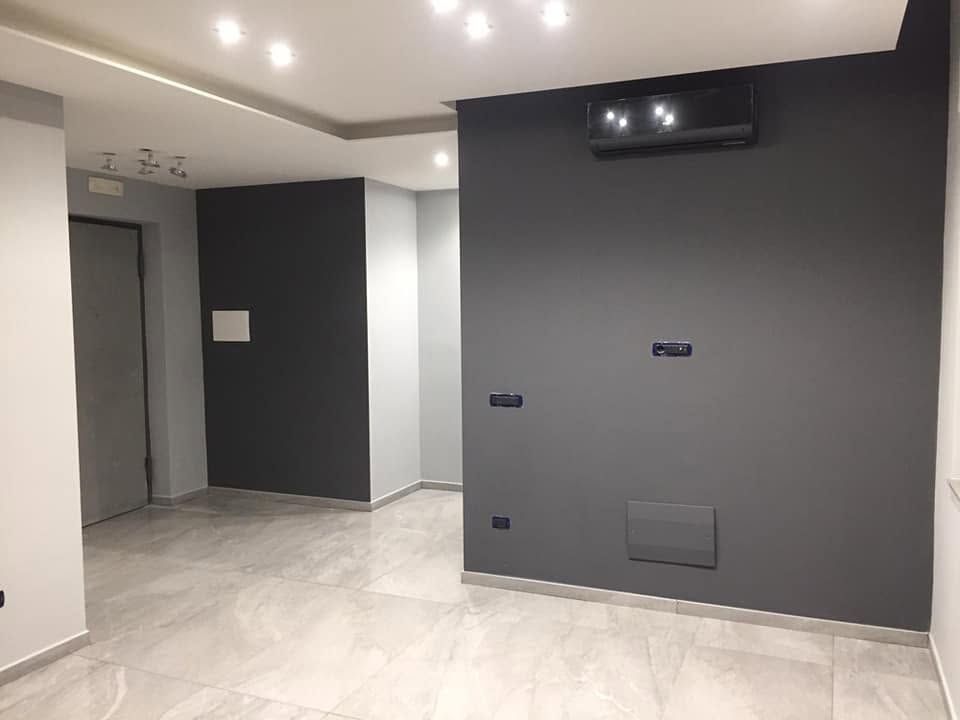 Stanza moderna vuota con parete d'accento grigia, pavimento piastrellato, faretti a incasso e mobile TV a parete.