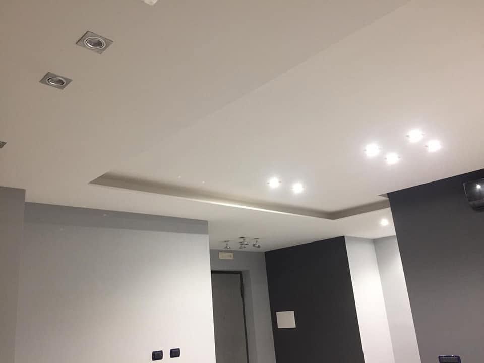 Interno moderno con faretti a incasso a soffitto, pareti grigie e una parete scura a contrasto in una stanza in fase di ristrutturazione.