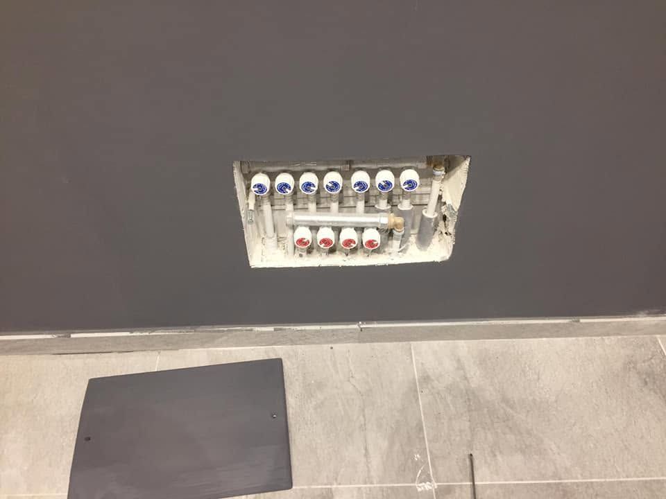 Pannello a muro con prese multiple sopra un pavimento piastrellato e un tappetino scuro su una parete grigia