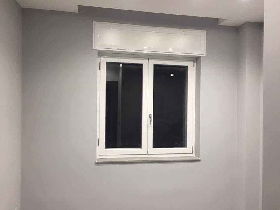Finestra con cornice bianca e tenda chiusa in una stanza grigio chiaro.