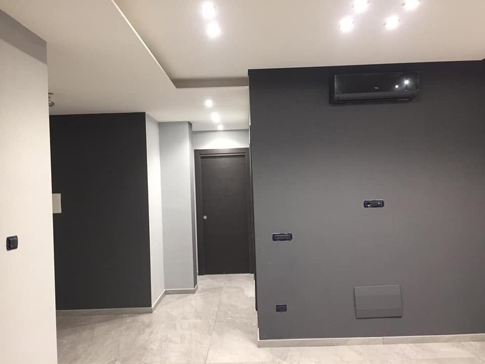 Interno moderno di una stanza con pareti grigie e nere, faretti a incasso a soffitto e condizionatore d'aria a parete.