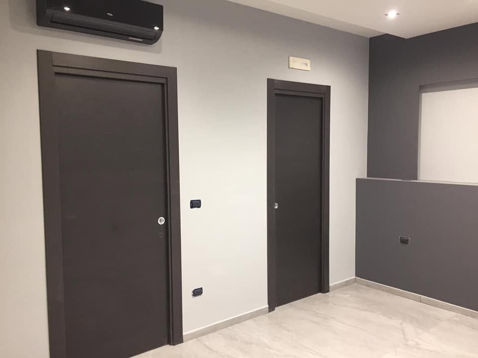 Camera moderna con due porte scure, pareti grigie, pavimento piastrellato e condizionatore d'aria sopra.