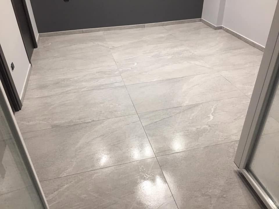 Stanza vuota piastrellata con pavimento grigio chiaro e pareti scure, vista attraverso una porta.