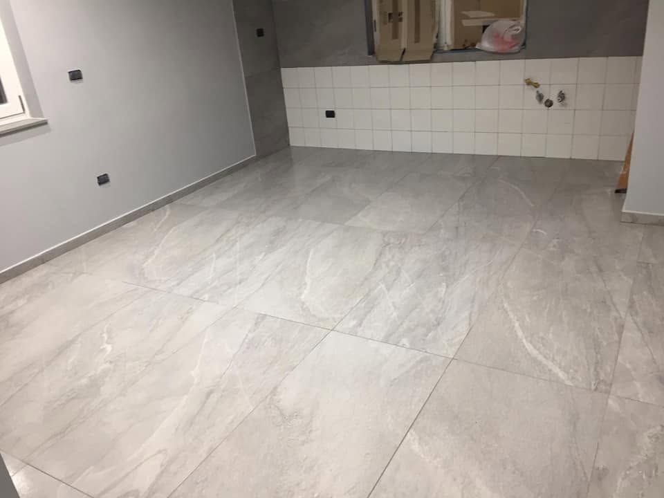 Stanza vuota con pavimento piastrellato grigio chiaro e rivestimento a parete piastrellato bianco in zona cucina.