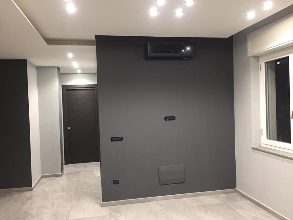 Stanza moderna vuota con una parete scura a contrasto, faretti a incasso sul soffitto e una finestra sulla destra.