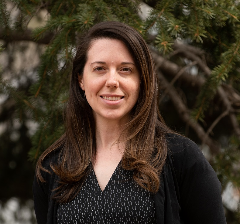 A woman is standing in front of a tree and smiling for the camera.