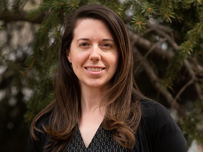 A woman is smiling for the camera in front of a tree.