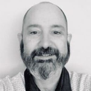 A bald man with a beard is smiling in a black and white photo.