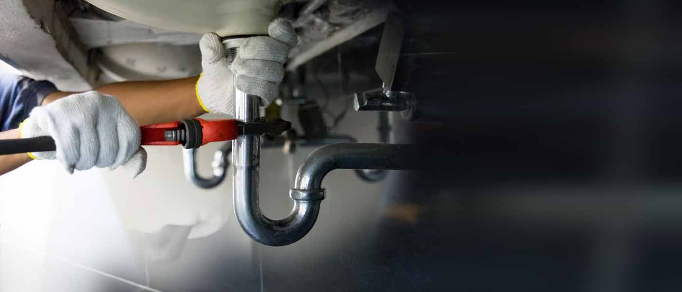 A plumber is fixing a sink with a wrench.