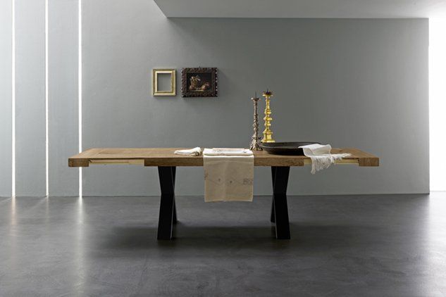 In una stanza minimalista, un tavolo da pranzo in legno con gambe nere a forma di X, decorato con un runner, candelabri e una ciotola.