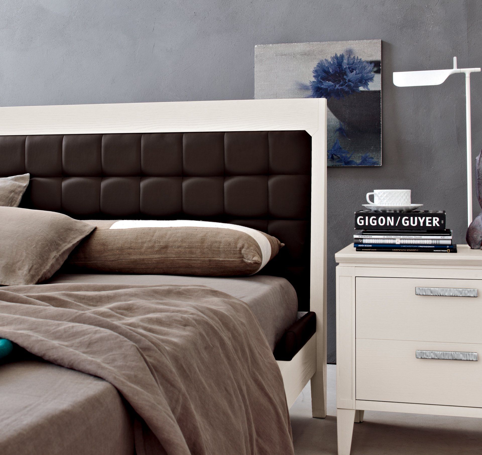 Una moderna camera da letto con un letto bianco con testiera imbottita marrone scuro e comodino bianco.