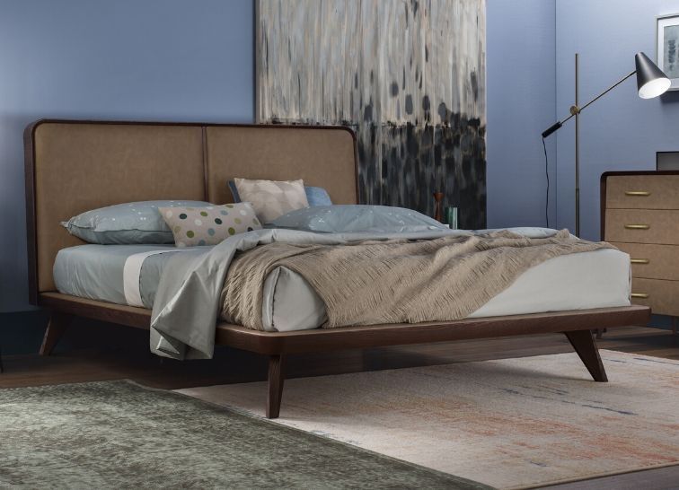 Un letto imbottito in stile moderno di metà secolo con testiera color cuoio e base in legno in una camera da letto con pareti blu.