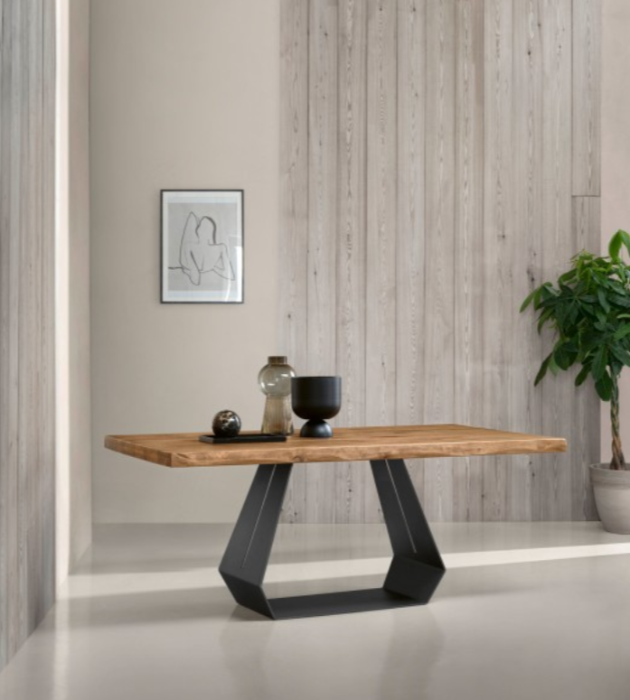 Un tavolo da pranzo in legno con base geometrica in metallo nero, addossato a una parete rivestita in legno chiaro con decorazioni e una pianta.