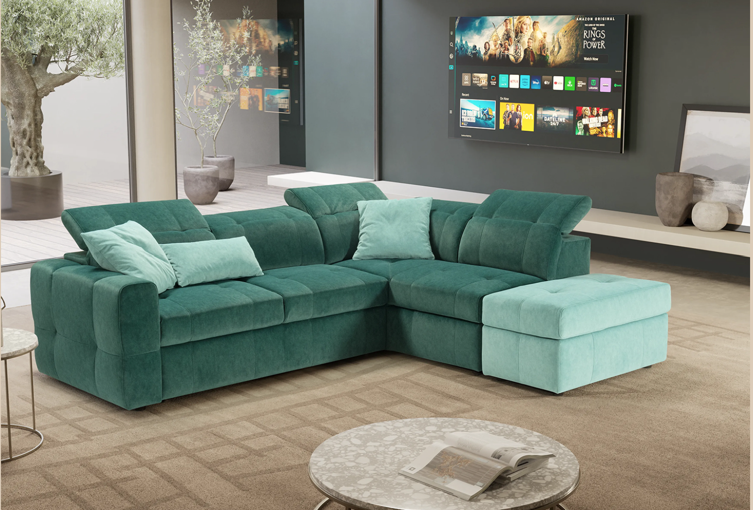 In un soggiorno moderno, con televisore e tavolino rotondo, si trova un divano angolare a L di colore verde con cuscini coordinati.