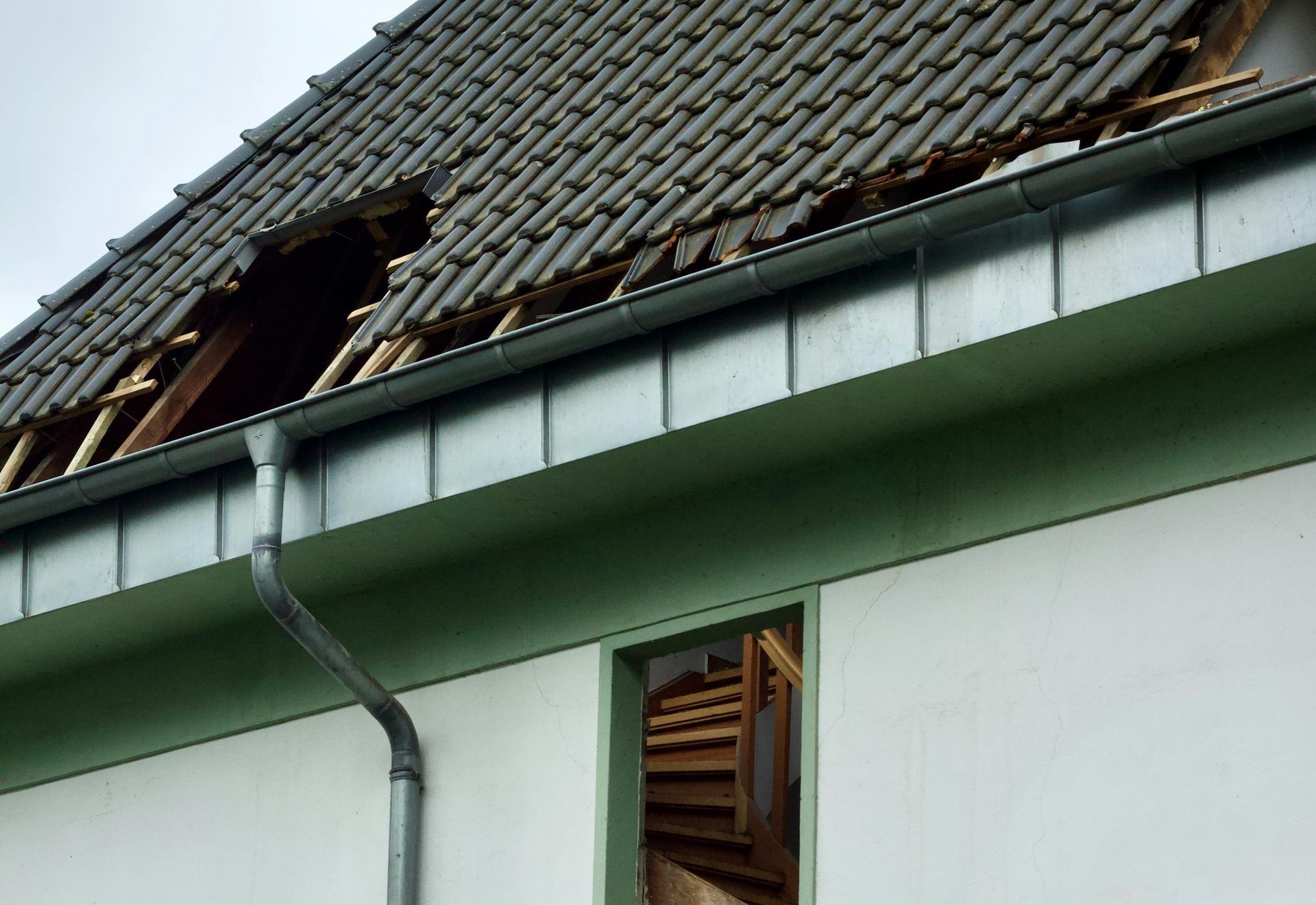 Damaged tiled roof with missing shingles and broken window on a house exterior in Central PA