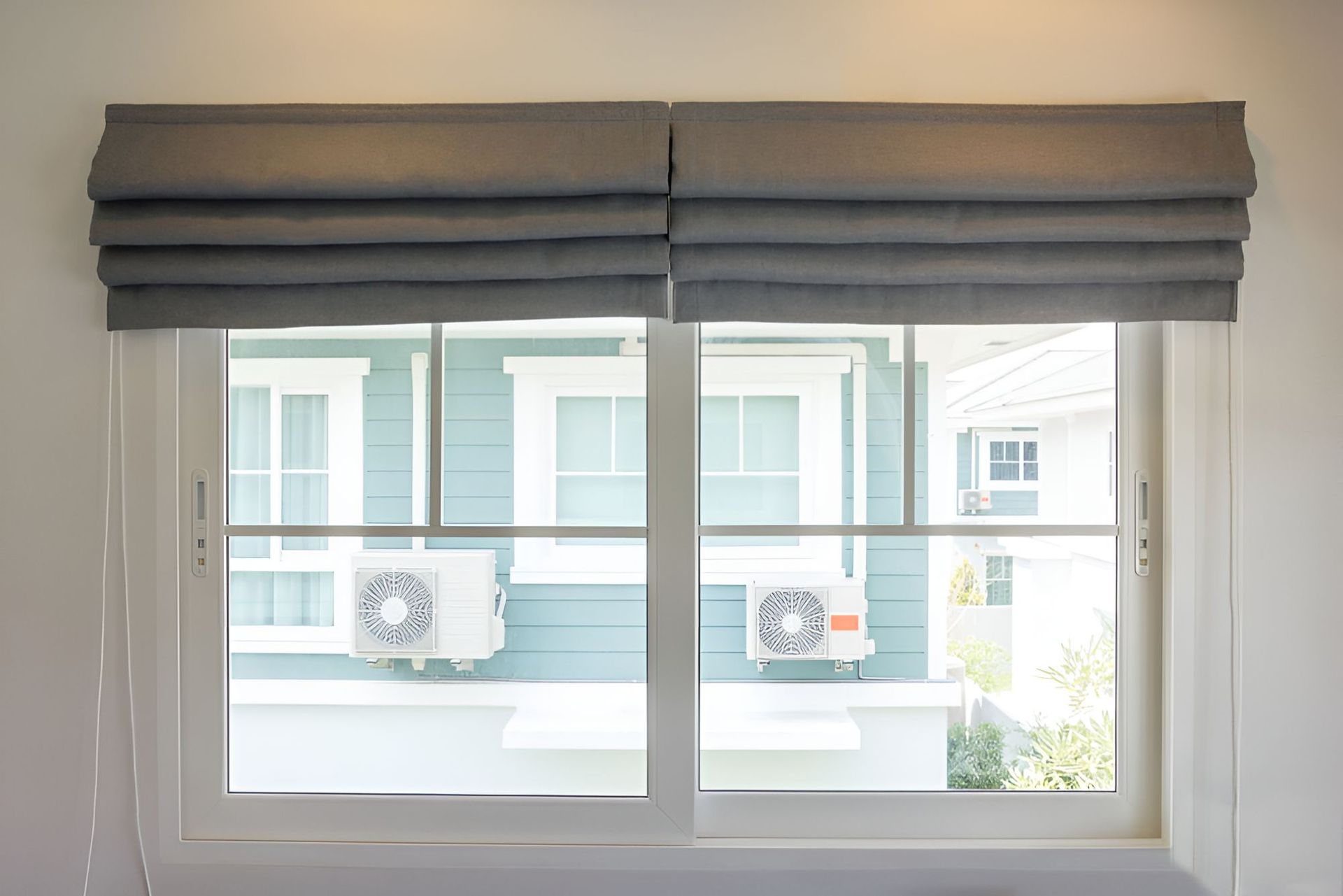 A Window With Roman Shades in a Room With a Blue House in the Background — Newcastle Curtains And Blinds In Warners Bay, NSW