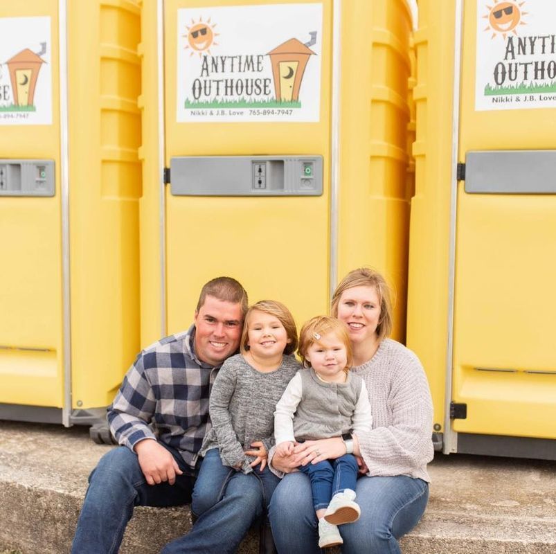 The Love family sitting in front of yellow portable toilets with Anytime Outhouse logo. 