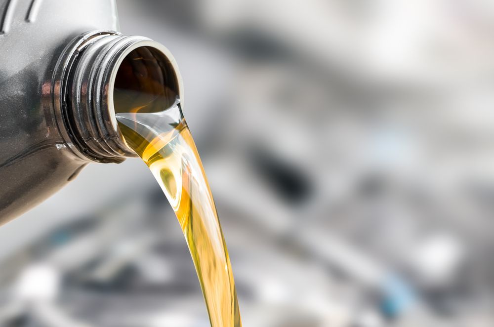 A Bottle of Oil is Being Poured Into a Car Engine — North Queensland Independant Fuel Services in Slade Point, QLD
