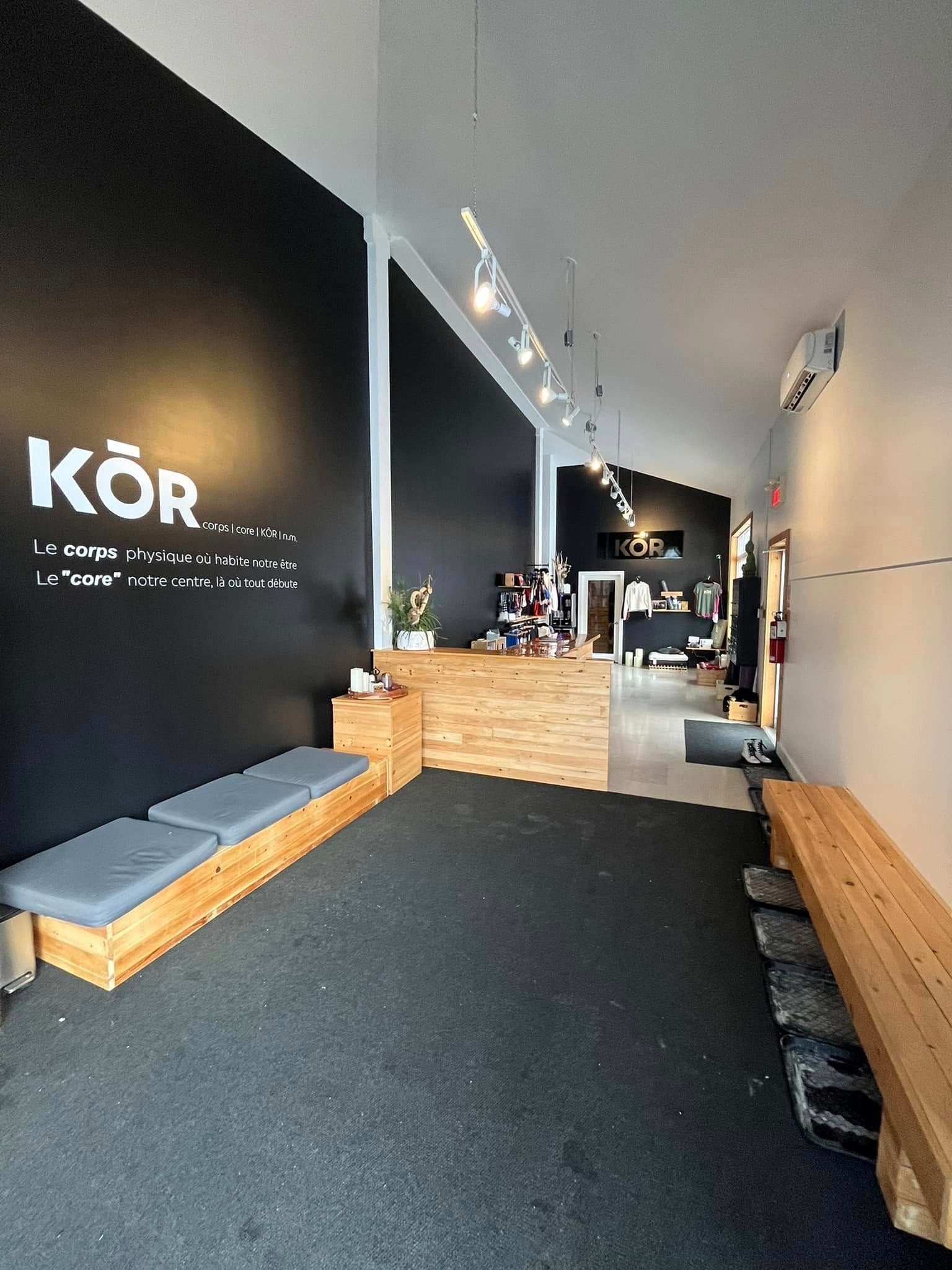 Intérieur d'un studio de fitness avec murs noirs et blancs, bancs en bois et comptoir d'accueil.