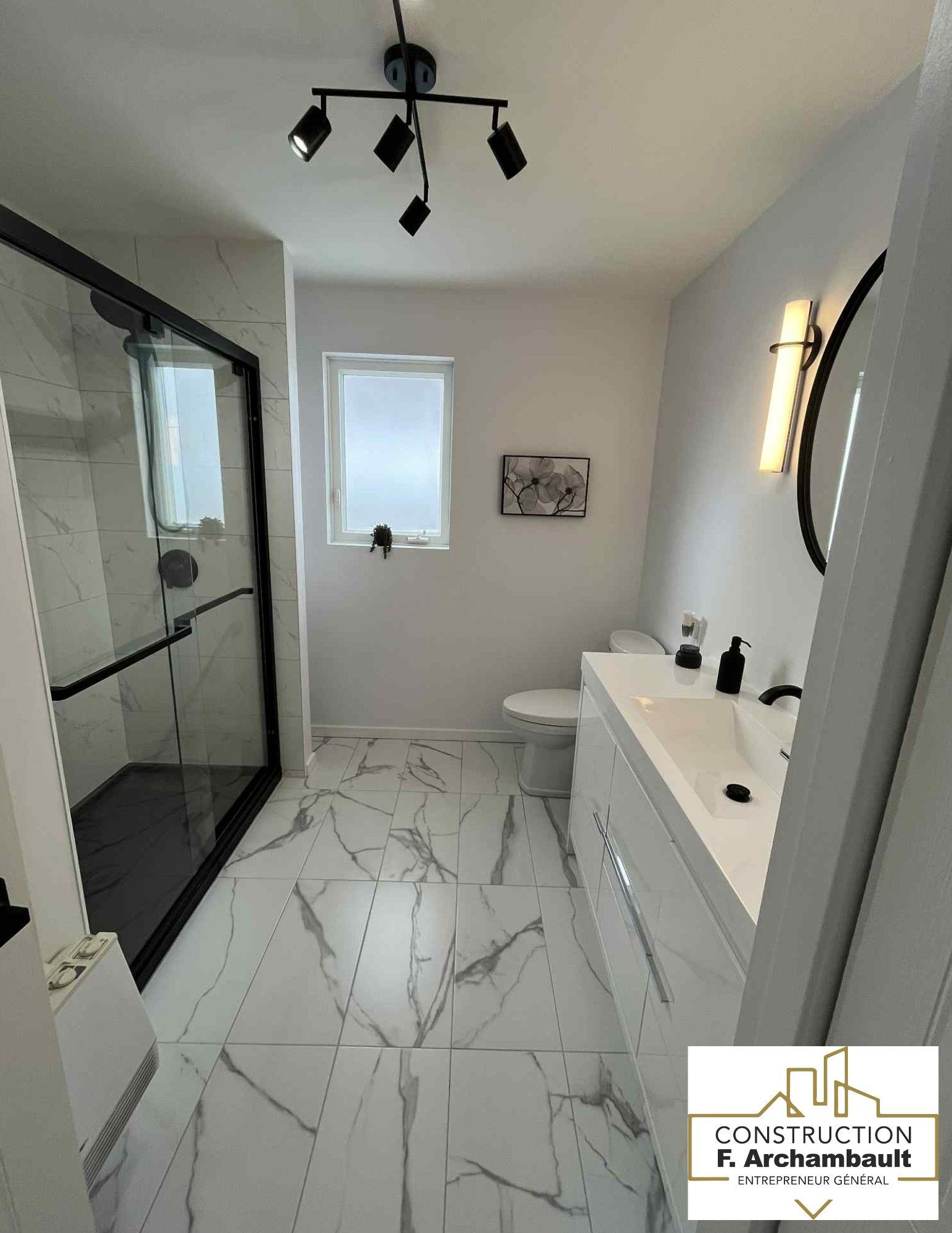 Salle de bains moderne avec carrelage blanc et noir, douche en verre, meuble-lavabo blanc et touches de noir.