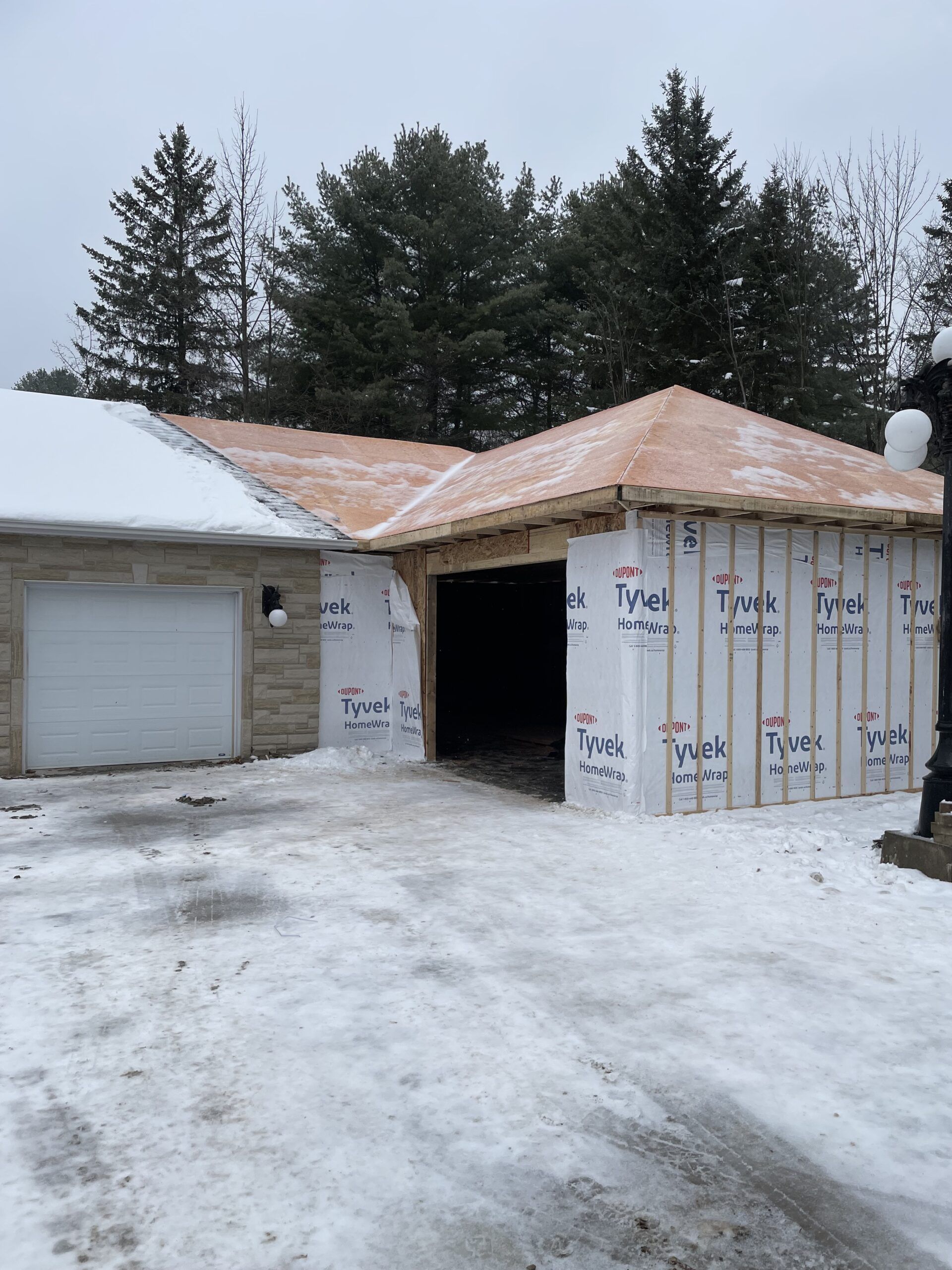 Garage en construction, charpente et revêtement en bois, allée enneigée, décor hivernal.