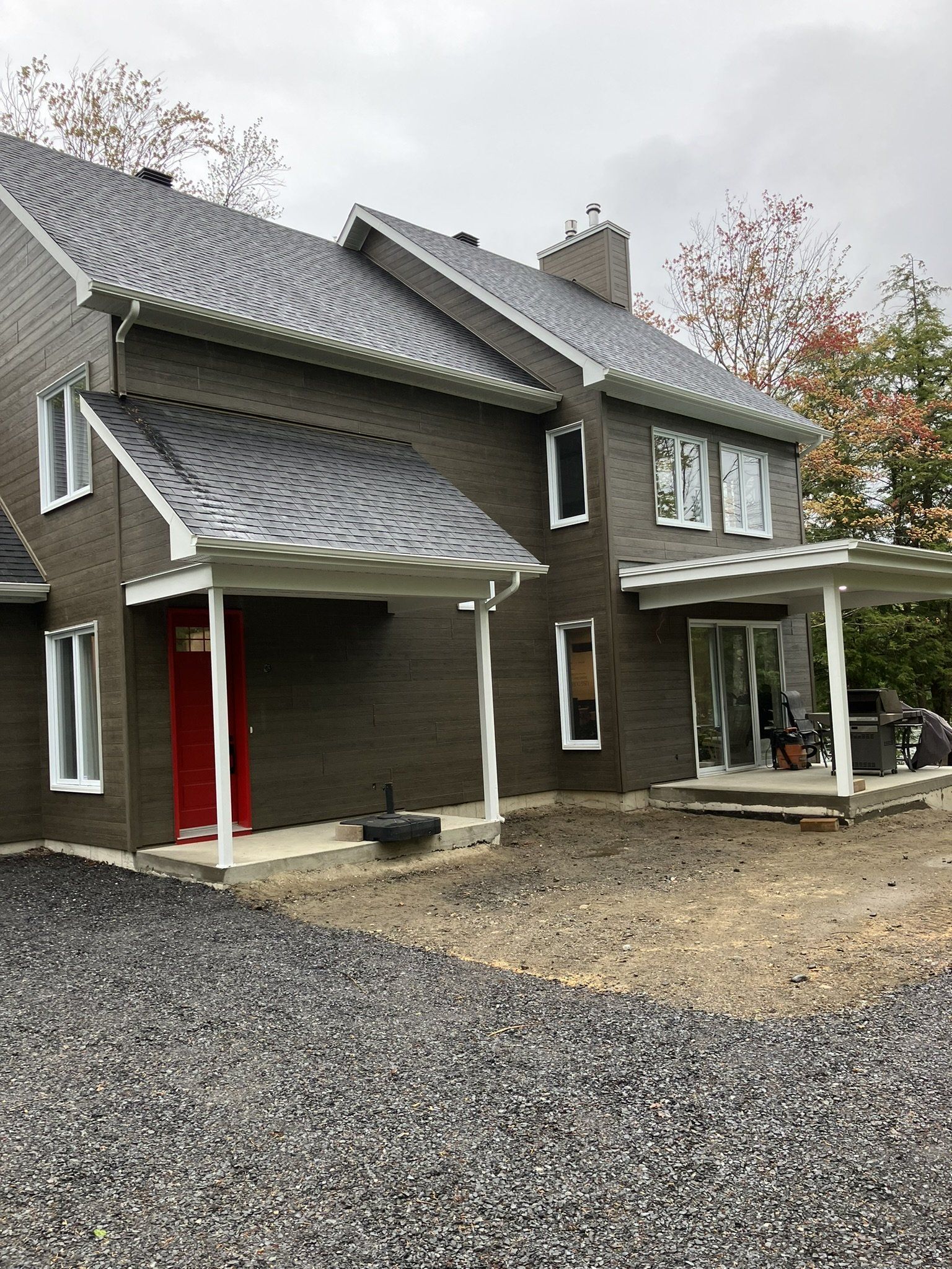 Maisons de ville en briques de deux étages avec porte rouge, entrées couvertes, allée de gravier et ciel couvert.
