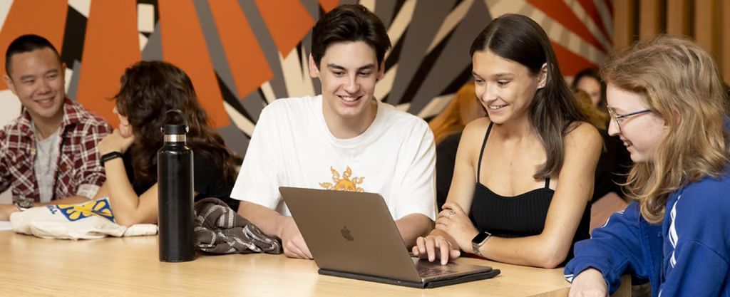 People gathered around a laptop in a modern office, smiling and collaborating at a table.