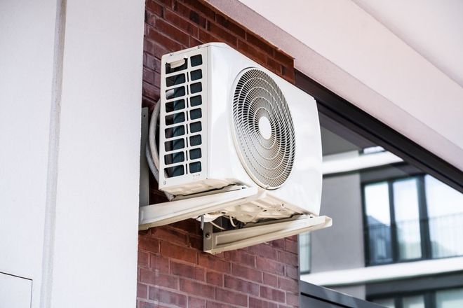 Outdoor air conditioner unit mounted on a brick wall under a building overhang