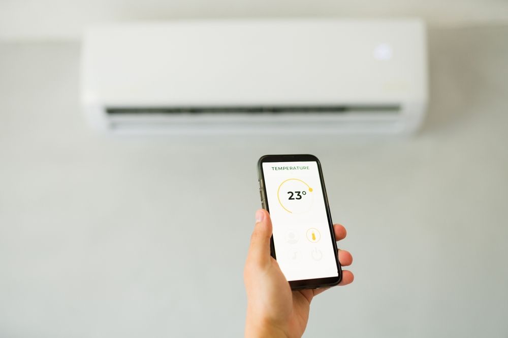 Hand holding a smartphone controlling a wall-mounted air conditioner set to 23°