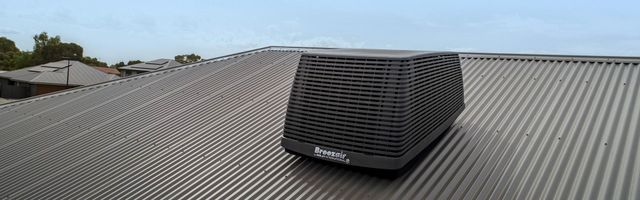Black rooftop HVAC unit on a corrugated metal roof under an overcast sky