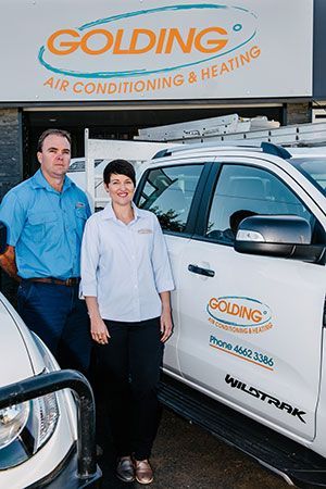Two workers standing beside a Golding Air Conditioning & Heating service truck outside the shop