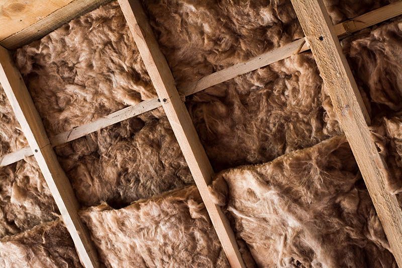 Wooden roof framing with brown insulation batts between rafters