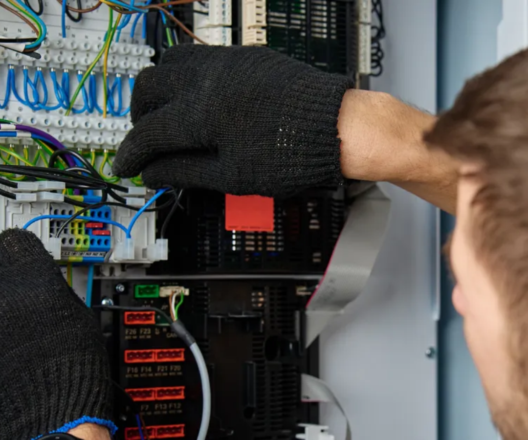 Gloved hands working inside an electrical control panel with wires and circuit breakers