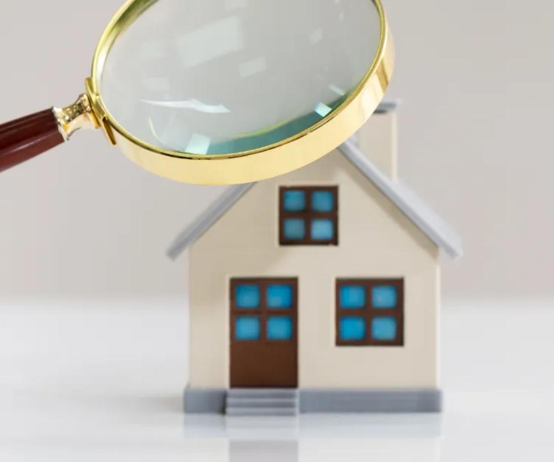 Magnifying glass over a small house model, suggesting home inspection or property search.