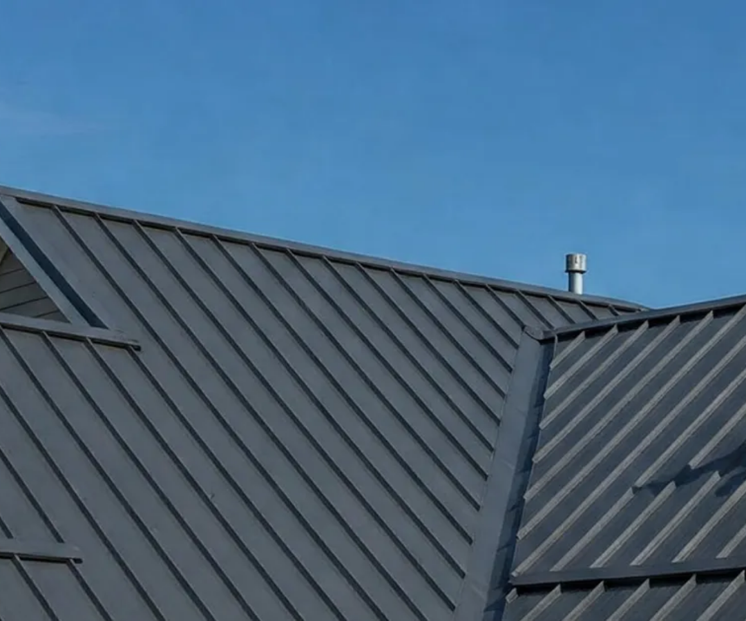Dark gray metal roof panels against a clear blue sky, with a small vent near the ridge.
