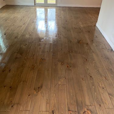 Polished wood floor reflecting light from a window. The wood is light brown with visible grain and knots.