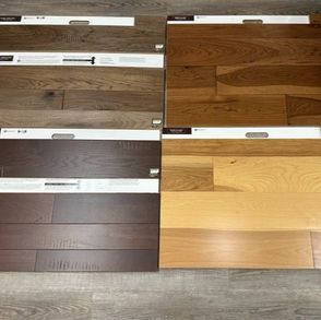Four wood floor samples in different shades of brown and tan arranged on a gray surface.