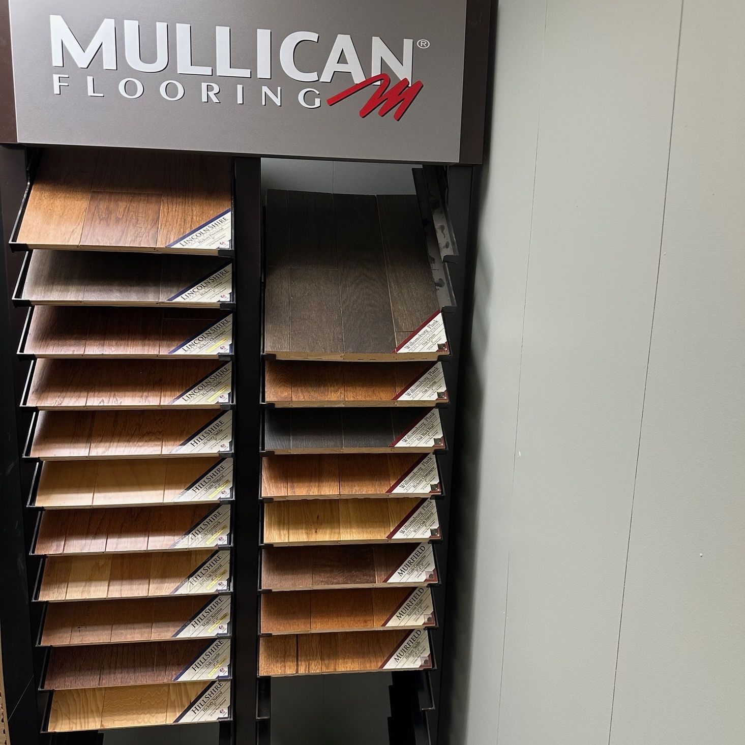 Display of various wood flooring samples by Mulllican. Dark brown stand with multiple color options.