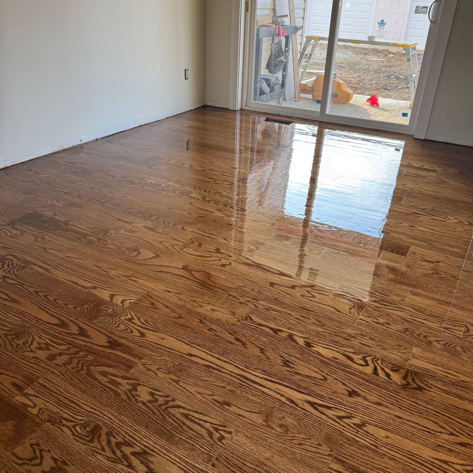 Refinished hardwood floor with a glossy finish, reflecting a window and the room.