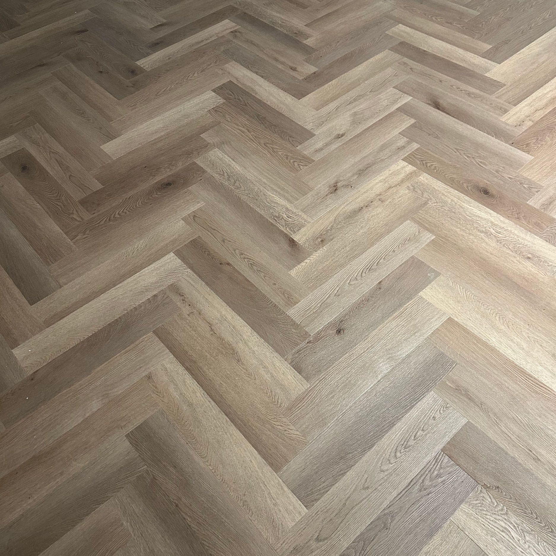 Herringbone pattern wooden floor. Light brown planks arranged in a zigzag design.