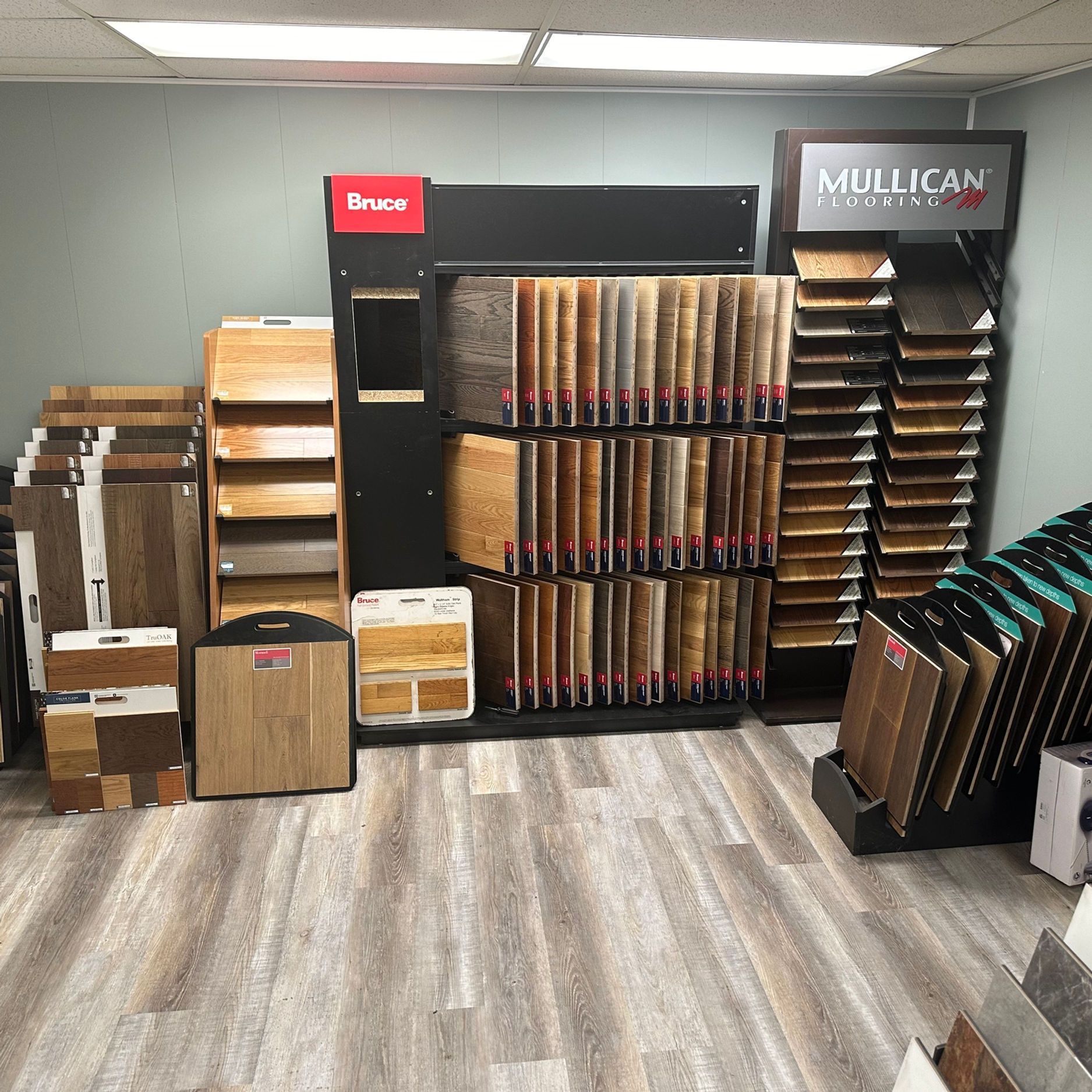 Flooring samples displayed in a showroom. Various wood, tile, and laminate options shown on the floor and stands.
