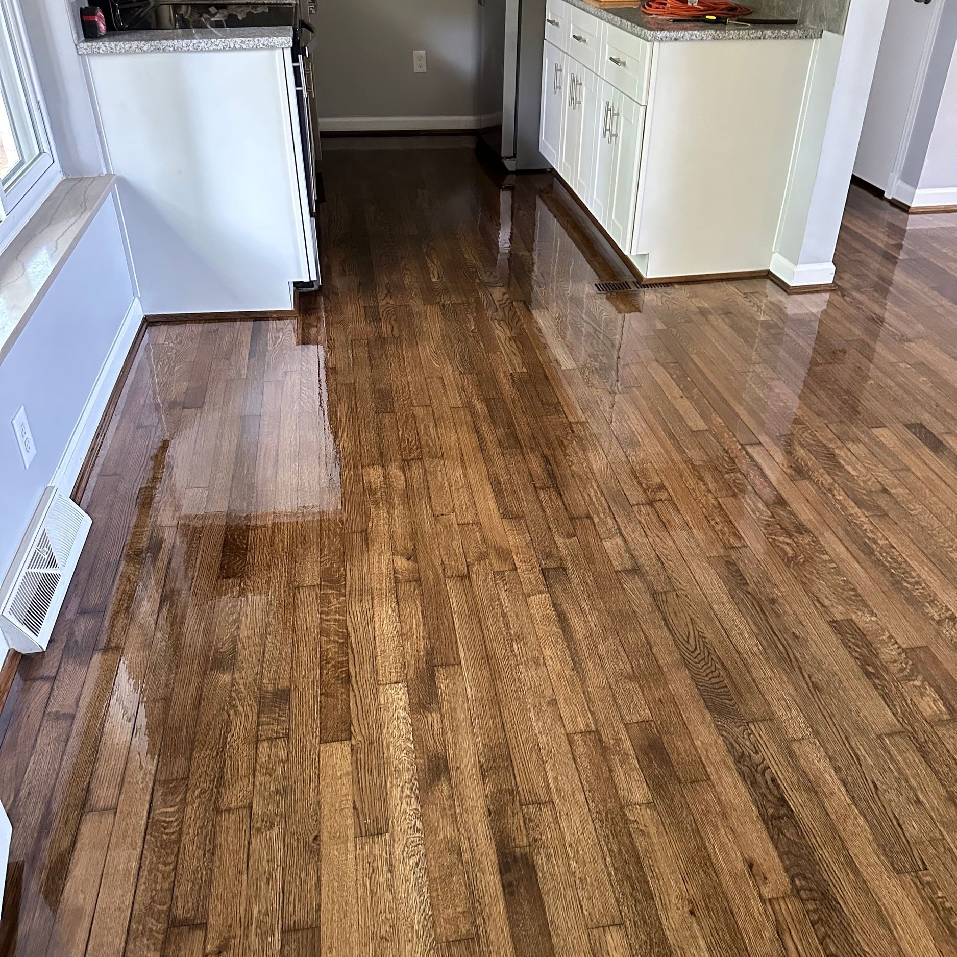 Wooden floor with a glossy finish in a kitchen with white cabinets.