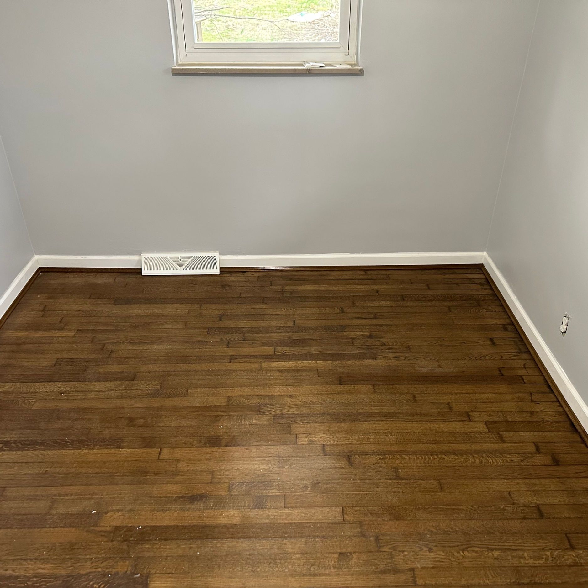 Empty room with dark wood floor, gray walls, white trim, and a small window at the top.