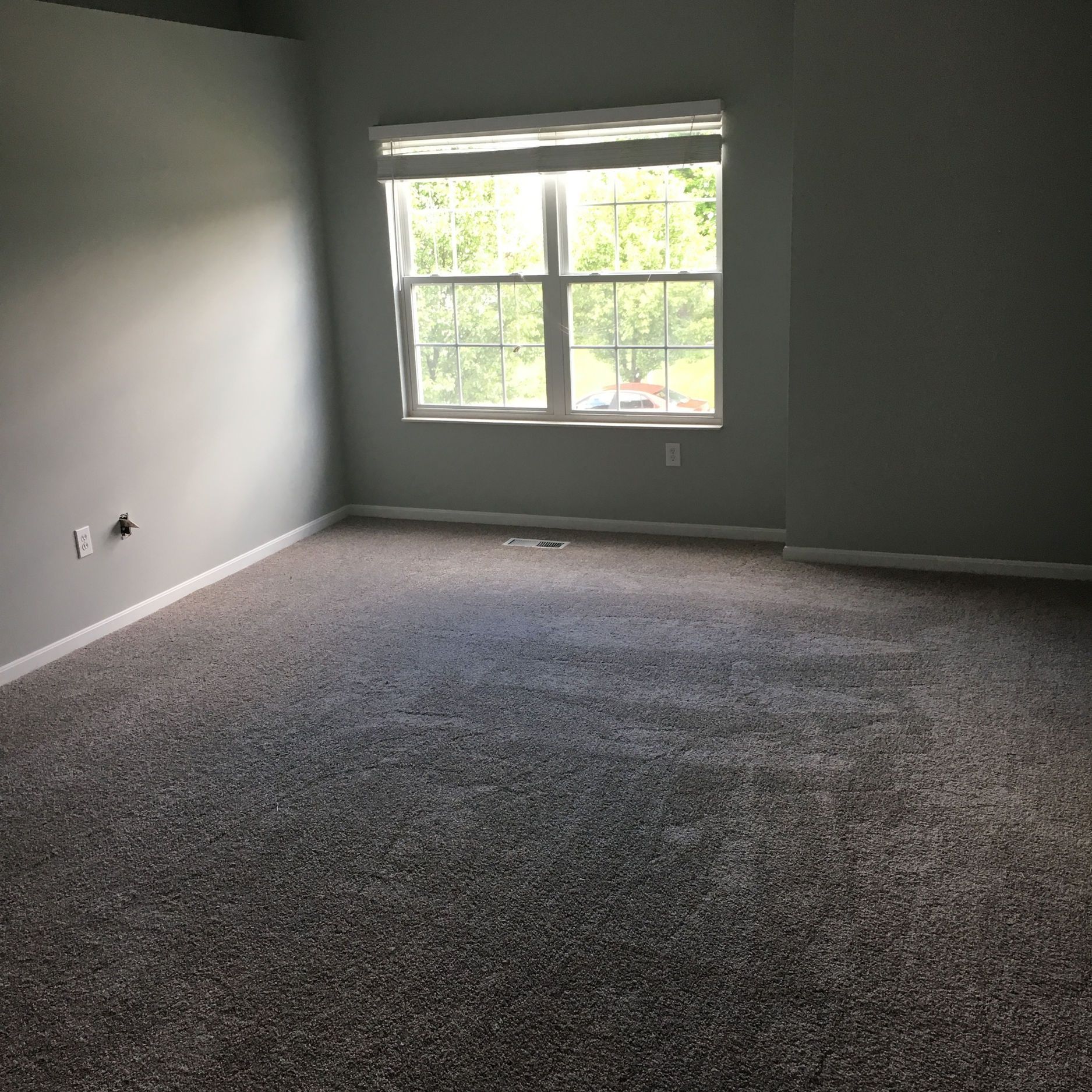 Empty room with gray walls, window, and speckled gray carpet.