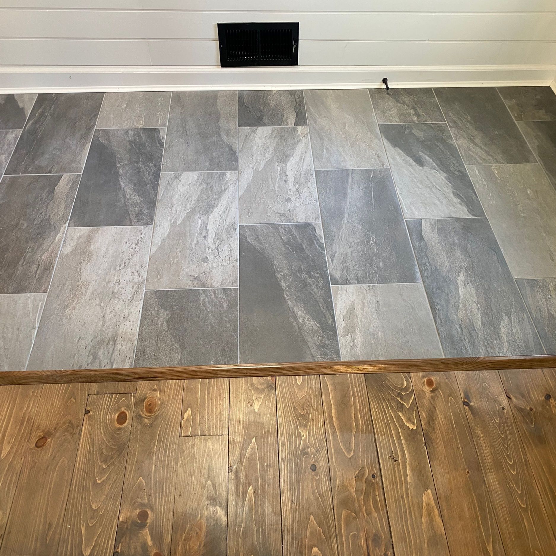 Gray tile flooring with wood plank border meets wooden floor.
